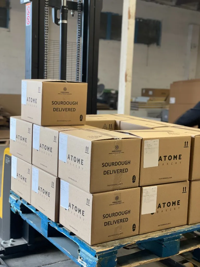 A pallet stacked with Atome Bakery 'Sourdough Delivered' shipping boxes in the F2C Vancouver warehouse